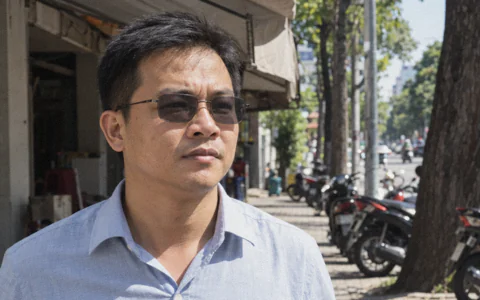 Người đàn ông đeo kính cận tròng đổi màu đã sẫm xám, bước ra vỉa hè đầy nắng buổi sáng